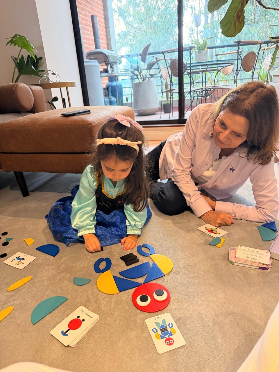 A grandmother and her granddaughter sitting on the floor together solving a colourful puzzle